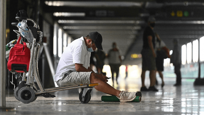 un viajero espera sentado en el suelo de un pasillo del aeropuerto de madrid barajas