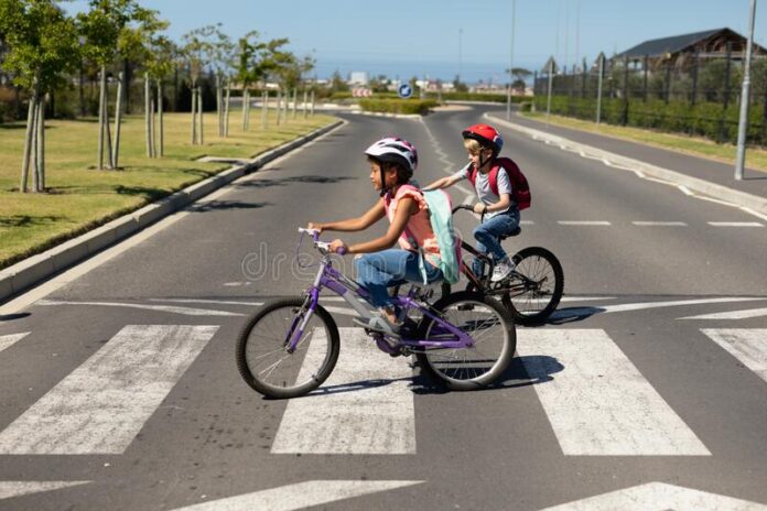 escolares cruzando la carretera con bicicletas vista lateral de una colegiala caucasica y afroamericana ambas cascos en bicicleta 169966635